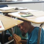 Sophomore Maggie Kaliszak laughs while she gets under her desk during the drill.