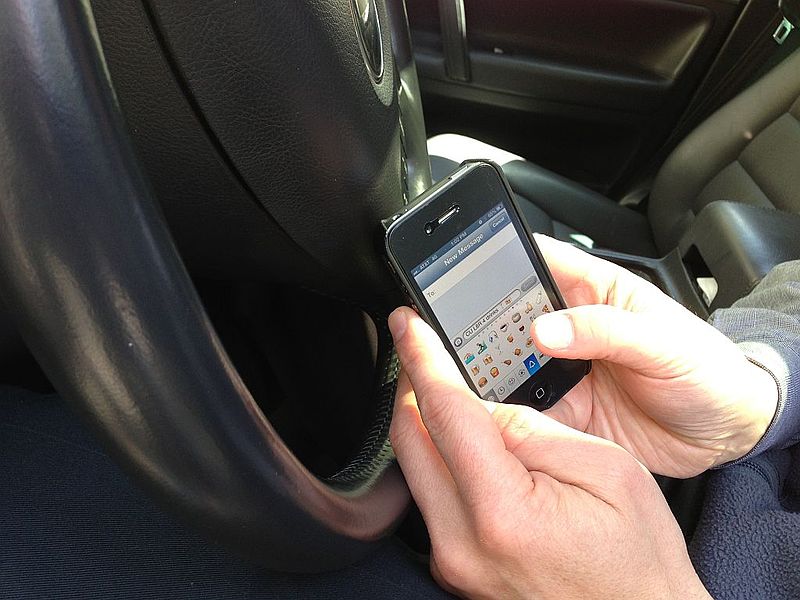 Though responding to a message while driving is tempting, it is unnecessary and dangerous. Photo by Intel Free Press [CC-BY-SA-2.0 (http://creativecommons.org/licenses/by-sa/2.0)], via Wikimedia Commons; phone and wheel