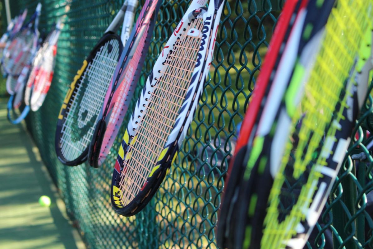 Tennis rackets are hung on the fence while the team goes into the huddle. Photo By: Jade Reall