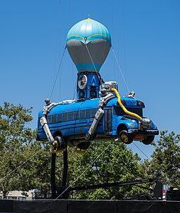 A real life battle bus floats in the air mimicking an animated one with 100 players ready to jump out.
Photo by By Sergey Galyonkin from Raleigh, USA (Fortnite Pro-Am 2018) [CC BY-SA 2.0  (https://creativecommons.org/licenses/by-sa/2.0)], via Wikimedia Commons