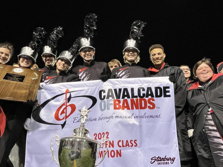 Marching band members huddle around their championship trophy and banner. 