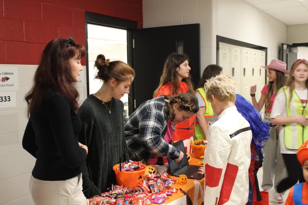 Trick-or-Treaters at the Aevidum club table receive candy and spin a game wheel.  Aevidum members created a spin-the-wheel activity in which children would spin it to learn about different coping mechanisms. They could try and receive an extra piece of candy as a reward. Sophomore Maria Agostino hopes the activity will influence students and parents to know what to do when they are struggling. “Aevidum did really well, Agostino said. Our coping skill wheel was a way to help the kids…[figure out] ideas for when they may be stressed or overwhelmed [and] to put these coping methods into their everyday life. The parents seemed to really like the idea, and it helped them recognize what they could do to help when their kid was struggling.” Photograph Courtesy of Kendall Woods 