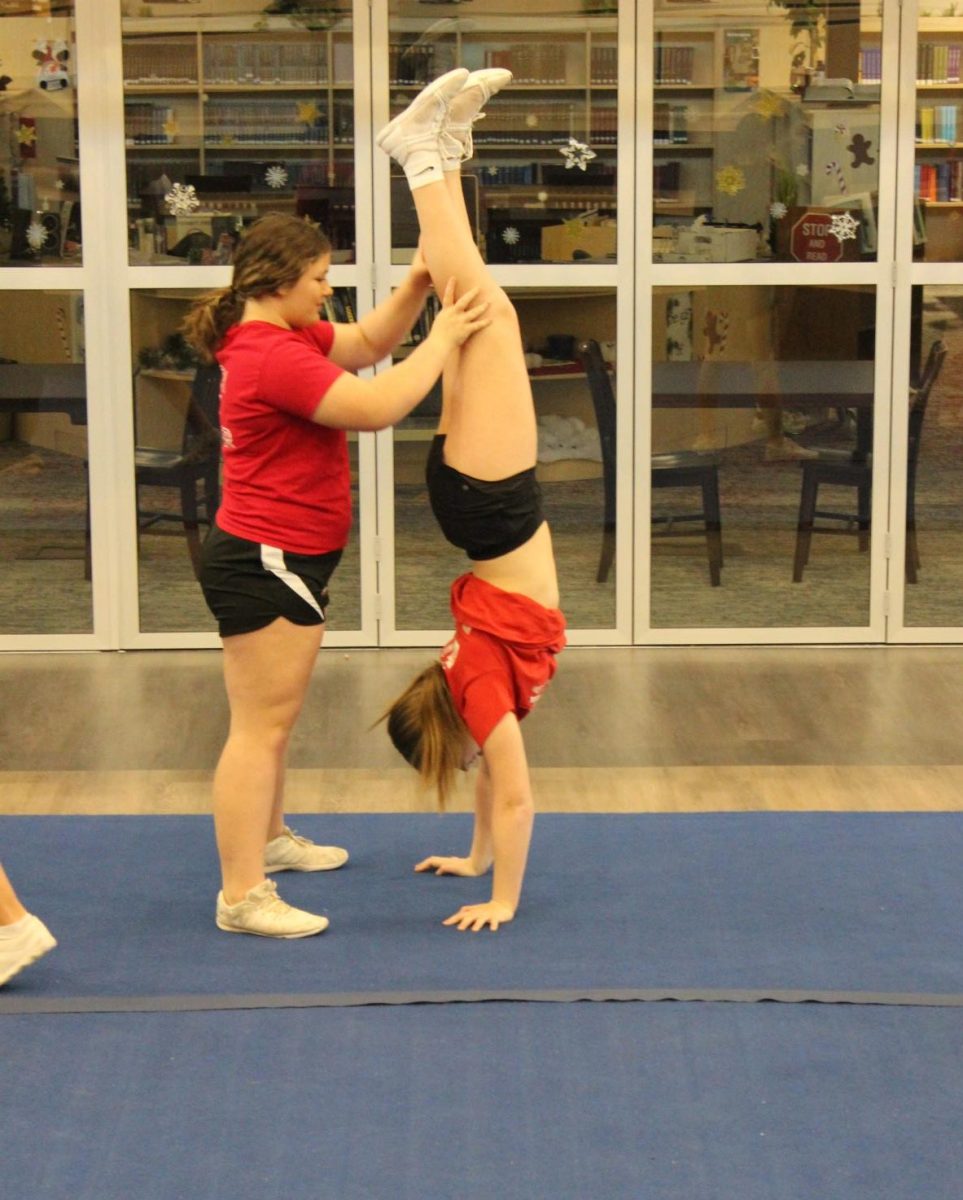 Freshman Bella Bauer and sophomore Joie Phillips perfect Bauer´s handstand during a practice in mid-December. The cheer team uses many techniques to memorize the choreography of their routines; however, for some, like senior Arielle Wilson, practice and repetition are the answer. I personally do not have any techniques for remembering choreography or anything,  Wilson said. For me, I think that it is all about the dedication, practice, and hard-work you put in which allows one to thrive. 
Junior Cassidy Derkosh appreciates how the captains use technology to help the girls. To memorize choreography, I ask my captains about the motions if I am not 100% sure about it, Derkosh said. Another thing I do is watch the videos they have sent out of each cheer. Photograph by Natalie Womack