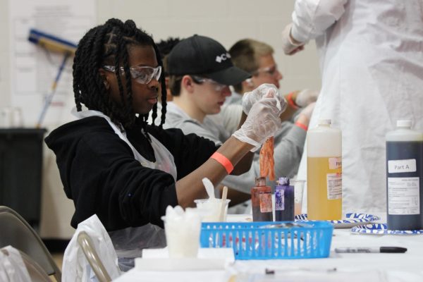 On Tuesday, March 5, 2024, after many delays, freshmen students at Susquehannock High School participated in a STEM day hosted by South Central PA Junior Achievement. Students participated in many activities demonstrating the four pillars of STEM, Science, Technology, Engineering and Math.
Freshman De’Jon Spriggs puts chemicals together in a hand at the chemistry station. Students were asked to mix chemicals to make polyurethane, which expands and fills a glove to make a hand.
