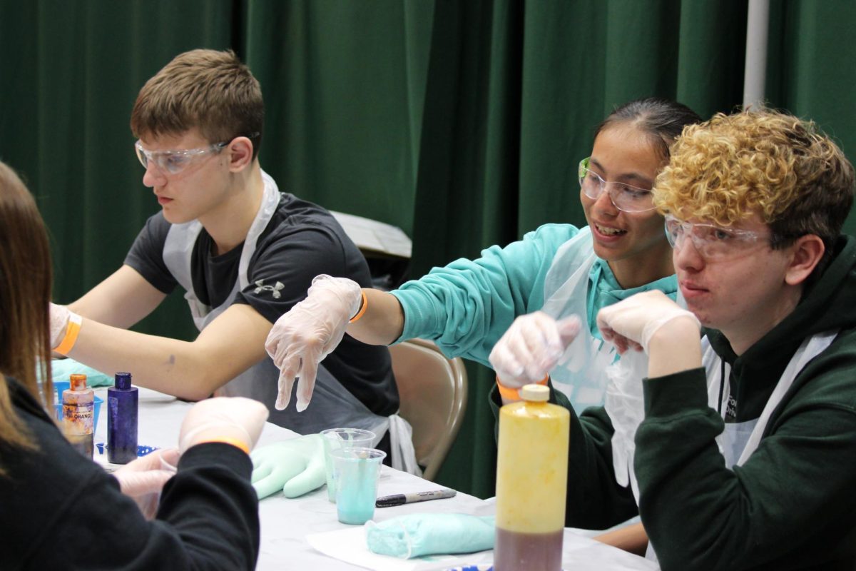 Freshmen Emerick Matuski, Chaske Hill and Travor Jarvis work with chemicals to create their polyurethane hands at the chemistry station. In this photo, they had just put the mixture into the hand and are waiting for the hands to expand.
