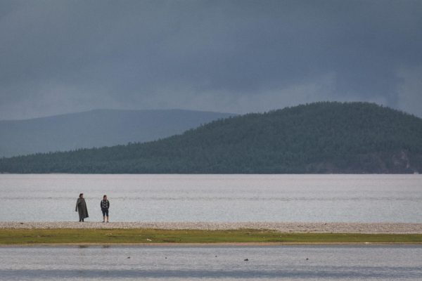 Photo of a beach, where people walk by a lake.