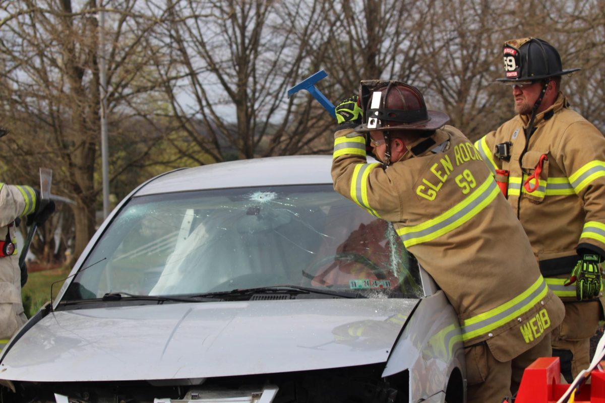  Glen Rock firefighters demonstrate how to safely access the interior of a vehicle by breaking the windshield. 
When a person is trapped in a vehicle, especially after a collision, breaking the windshield (or other windows) is a rapid way to access the victim for rescue and medical care. Firefighters use specialized tools and techniques to minimize damage and keep the broken glass away from the person being rescued.  Photograph by Peyton Elmore

