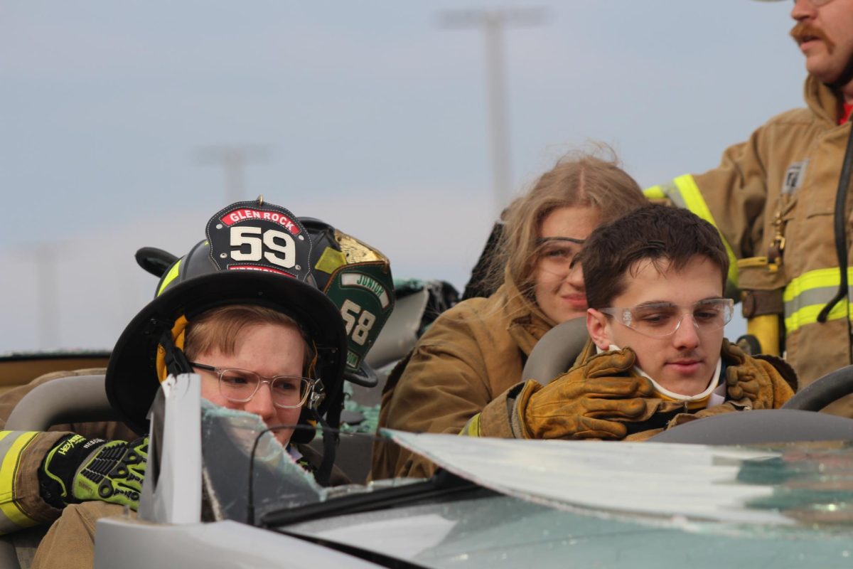  Students from the E.M.T. training class work to support the necks of students portraying the patients in a mock wrecked car. Supporting someone's neck after a car crash is crucial to prevent further injury and potentially catastrophic outcomes. It's important to immobilize the neck to protect the spinal cord and minimize the risk of paralysis or other spinal injuries.  Photograph by Peyton Elmore 
   
