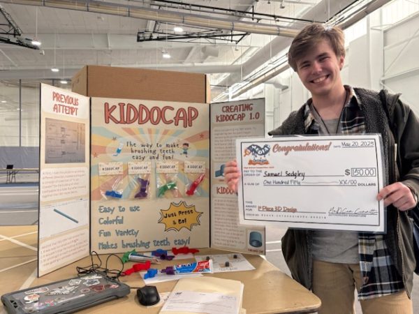 Junior Sam Sedgley presents his winning check in front of his creation, the KiddoCap. Photo courtesy of JC Lewis. 