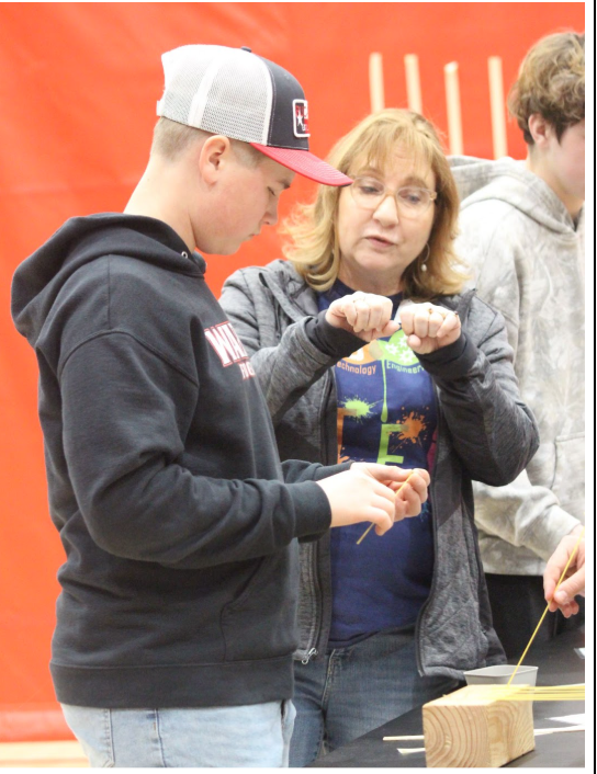 Freshman Cooper Myers works with a volunteer in learning how to build a bridge out of spaghetti noodles. The goal for students is to balance a little bowl of screws on the bridge. Photography by Josie Witsik