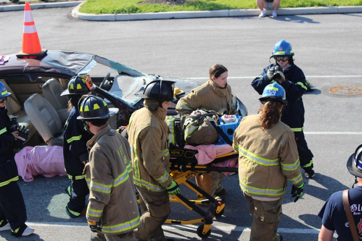EMT students carefully move ‘patient’ Aliva Crouse to the ambulance on the stretcher while  firefighters watch to ensure proper safety measures.  This training exercise has become a yearly tradition for the EMT class students to get hands-on experience working with local EMS personnel.

This training exercise has become a yearly tradition for the EMT class students to get hands-on experience working with local EMS personnel. Photograph by Peyton Elmore
